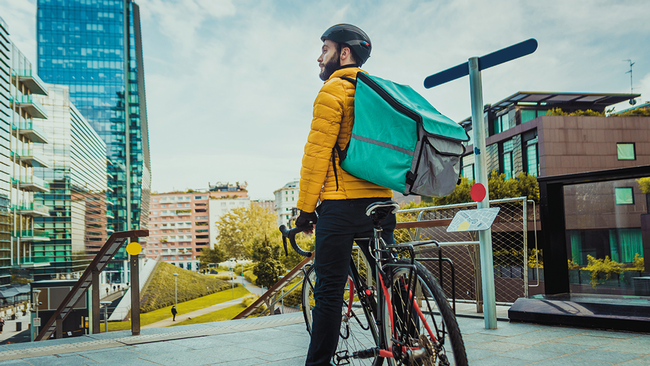 Fahrradbote steht vor Skyline © oneinchpunch, stock.adobe.com